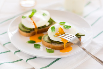 Vegetarian breakfast: avocado toast with poached eggs, orange juice, yogurt and jam on white wooden background. Selective focus