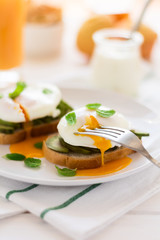 Vegetarian breakfast: avocado toast with poached eggs, orange juice, yogurt and jam on white wooden background. Selective focus