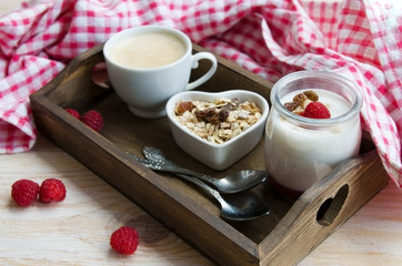 Fruit on the bottom yogurt jars,  muesli  and coffee on wooden tray with red check napkin. Yoghurt with raspberry jam and cappuccino. Concept for healthy eating or breakfast.
