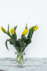 Bunch of yellow tulips in vase on wooden table