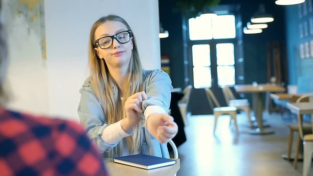 Blonde girl is rolling up sleeves while talking with her friend in the cafe
