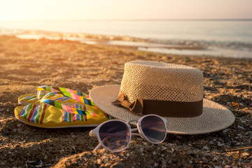 Hat with sunglasses on sand. Flip flops near the sea. The beach is calling. It's time to relax.