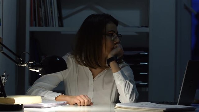 Tired businesswoman sitting at desk in front of laptop and checking time at her workplace
