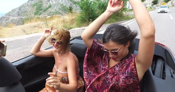 Two happy girls partying while riding in cabriolet