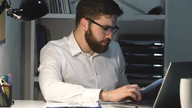 Young busy business man going through paperwork while sitting at office
