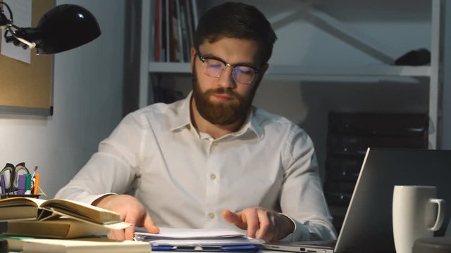 Tired overworked male employee stuck with paper work at office late