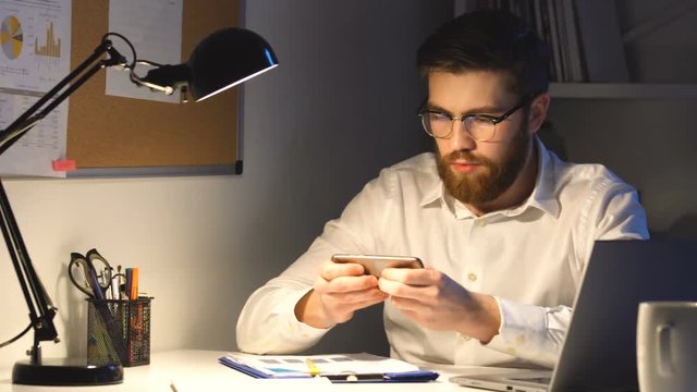 Silly young employee playing games on mobile phone in office instead of working hard