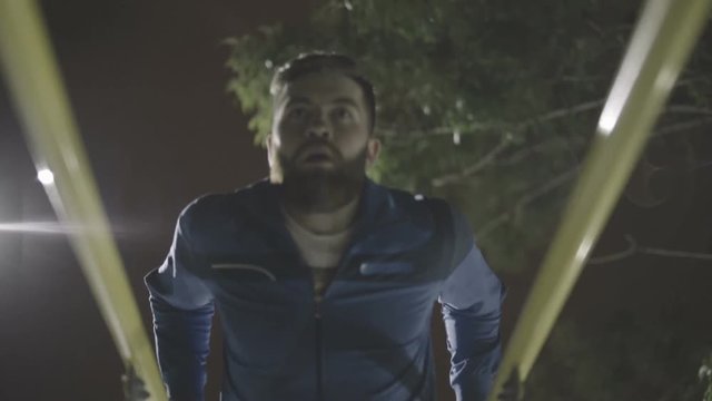Young bearded man doing exercises on parallel bars at a sports playground 