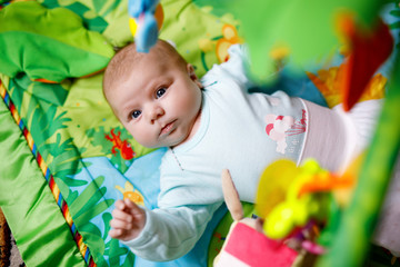 Fototapeta na wymiar Cute adorable newborn baby playing on colorful toy gym