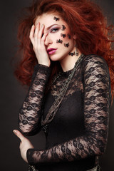 Fashion portrait of a beautiful red-haired woman with spiders on her face.