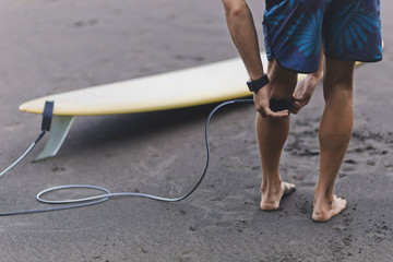 Surfer at the beach attaching surfboard leash