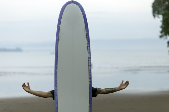 Man on the beach behind surfboard