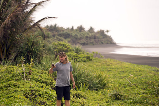 Indonesia, Java, man using cell phone at the coast