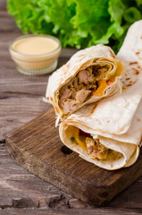 Shawarma chicken roll in a pita with fresh vegetables and cream sauce on wooden background. Selective focus