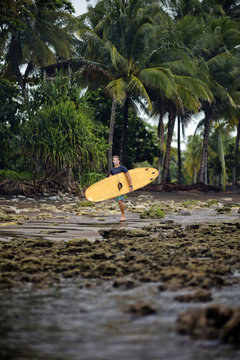 Indonesia, Java, man carrying surfboard at the coast