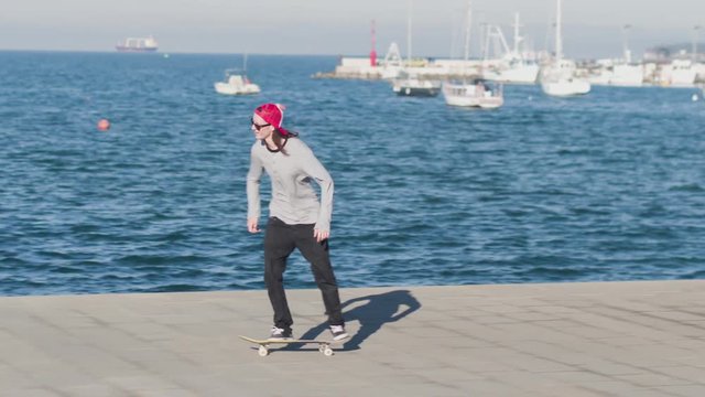 CLOSE UP: Young skateboarder skateboarding and jumping ollie flip trick on concrete oceanfront street on hot sunny summer day. Skateboarder boy jumping kickflip trick with skateboard at the seaside