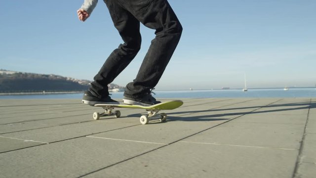 SLOW MOTION, CLOSE UP, DOF: Unrecognizable skateboarder skateboarding and jumping 360 flip trick on promenade along the ocean in sunny summer. Skateboarder riding skateboard jumping kickflip trick