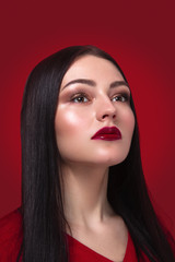 Fototapeta premium Beauty portrait of a young woman with creative makeup on a red background in studio