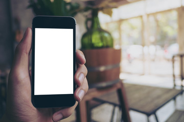 Mockup image of hand holding black mobile phone with blank white screen in vintage cafe