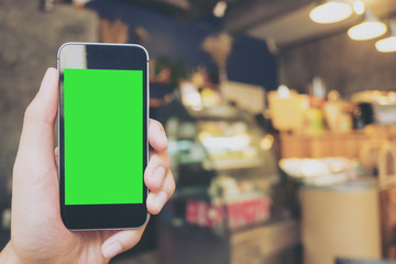 Mockup image of hand holding black mobile phone with blank white screen in vintage coffee cafe