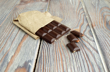 Плитка горького шоколада, завернутая в бумагу находится на деревянном столе
