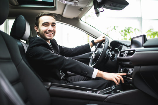 close up of young man in suit driving car and switching some button on panel of car