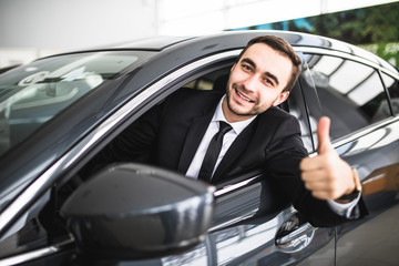 Fototapeta na wymiar Businessman smiling at camera showing thumbs up in his car