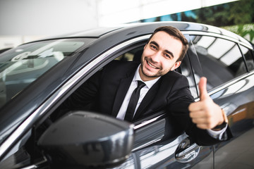 Businessman smiling at camera showing thumbs up in his car