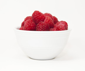 Red raspberries in a white bowl against a white background