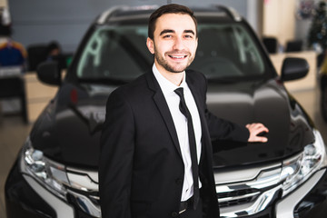 Fototapeta na wymiar Handsome young classic car salesman standing at the dealership in front of new car