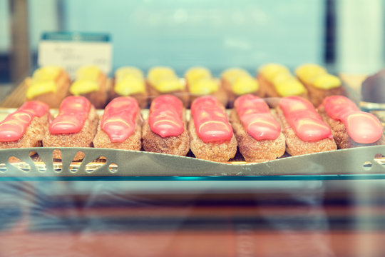 Many eclairs cakes on showcase in cafe. Eclairs with red and yellow glaze. Shallow depth of field. Toned.