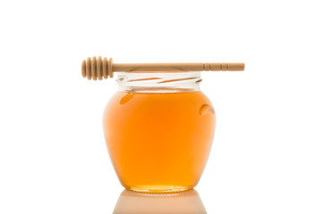 Glass jar full of honey and wooden stick on it isolated on a white background