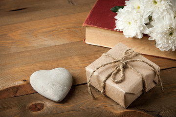 Gift box, old book, heart and flower on wooden table