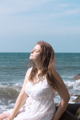 Fototapeta na wymiar beautiful girl on the beach in profile in a white dress smiling to the sun
