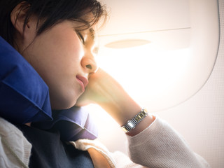 Tired asian lady napping with neck pillow plane.