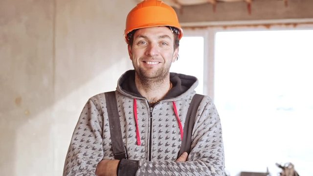 Middle-aged Caucasian male worker wearing orange hard hat standing with folded hands in slowmotion