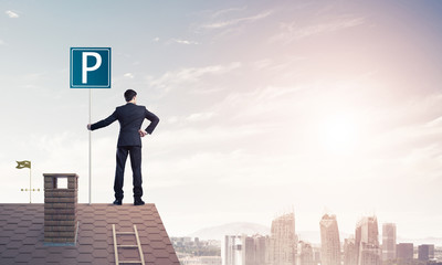 Young businessman with parking sign standing on brick roof. Mixe