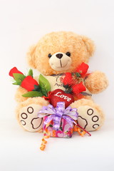 Brown teddy bear with a red rose and a gift box on a white background.