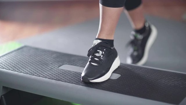 Close-up of female black athletic shoes stepping on a step platform. Woman engaged in fitness, using step-platform. Sport women's shoes. EMS