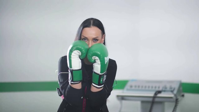 Woman in green boxing gloves hitting each other and began to boxing, imitating the blow. Woman boxing during EMS training. Woman engaged in fitness EMS.