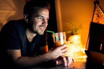 Cheerful man holding orange juice in right hand, surfing internet.