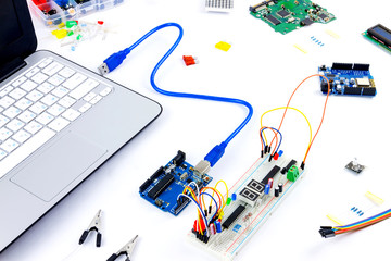 Microcontrollers, chips, resistors, usb cables and notebook on white desktop of hardware engineer. Engineer workplace