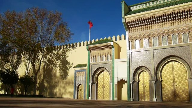 Left side of the Royal Palace of Fes (Dar el Makhzen), Morocco - golden doors, mosaics and red moroccan flag with wind. 