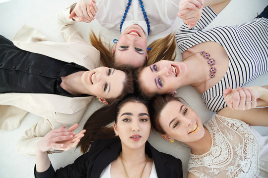 A group of joyful elegant girls lies in a circle, a top view, on a white background.