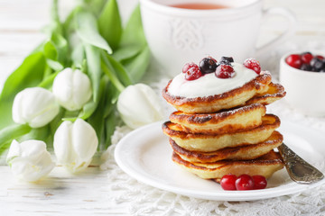 Breakfast. Fritters with sour cream and fresh berries. Pancakes. A Cup of tea, cranberries, black currant and flowers on the table. Selective focus