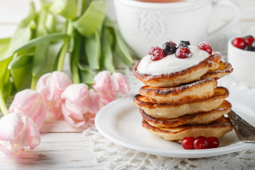 Breakfast. Fritters with sour cream and fresh berries. Pancakes. A Cup of tea, cranberries, black currant and flowers on the table. Selective focus