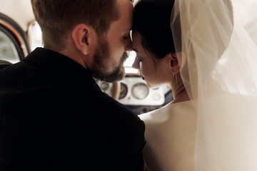 elegant gorgeous bride and handsome stylish groom gently hugging in car. unusual luxury wedding...