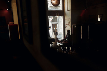 luxury wedding couple holding hands and sitting in cafe in morning near window in soft light. elegant gorgeous bride and stylish groom in retro style. romantic moment