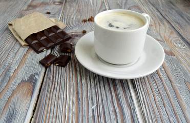 Чашка, наполненная с кофе, и  конфеты находятся на деревянном столе.
