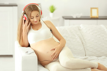 Young pregnant woman with headphones on the sofa
